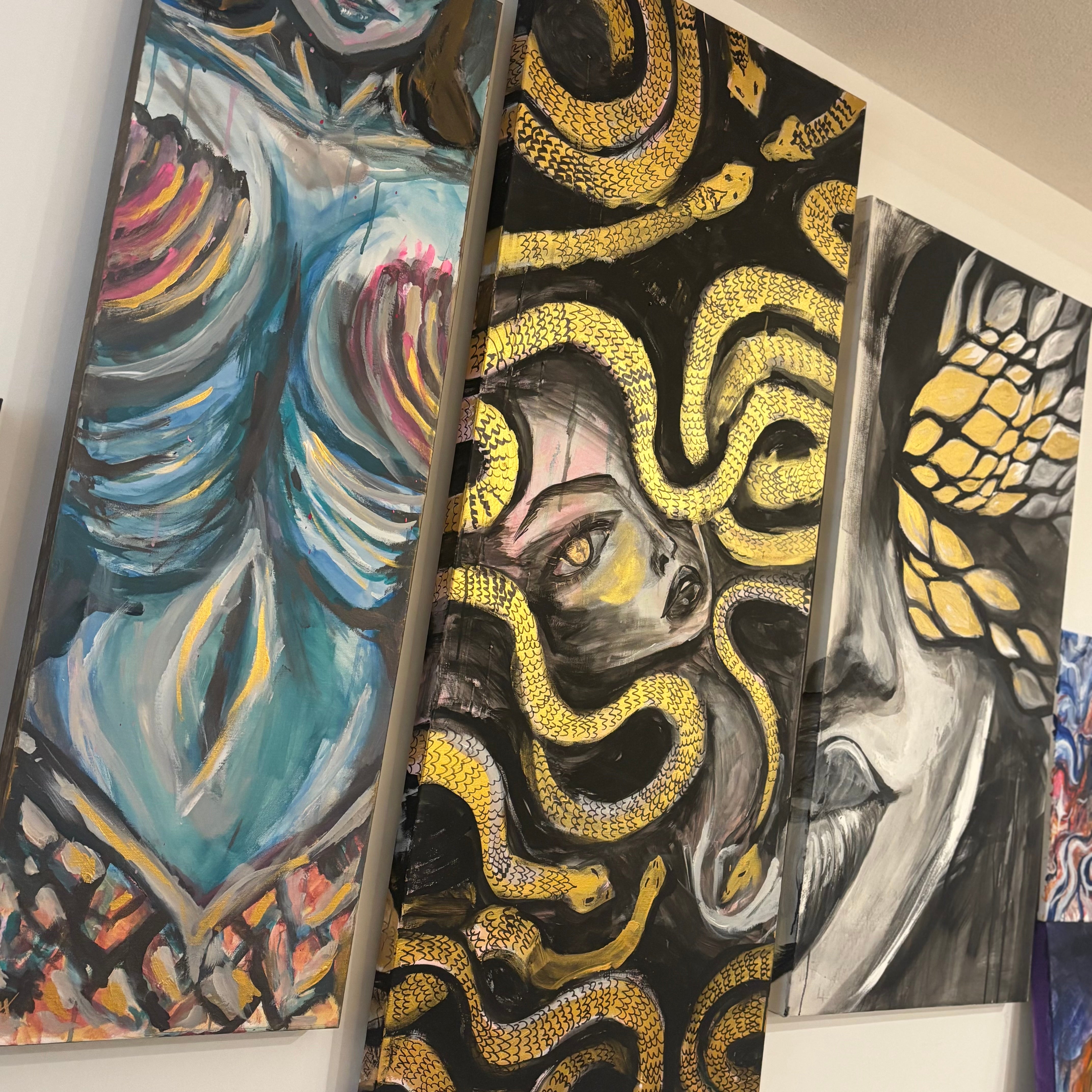 Photo of a gallery wall with 3 large narrow paintings. On the left, a mermaid painting, in the middle, the “medusa” painting, on the right, “metamorphosis"